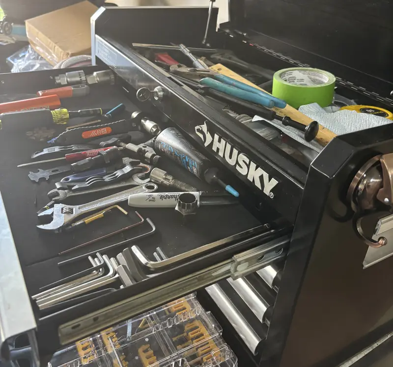 An open black Husky tool chest, its top drawer full of wrenches, hex keys, screwdrivers and a tube of grease.